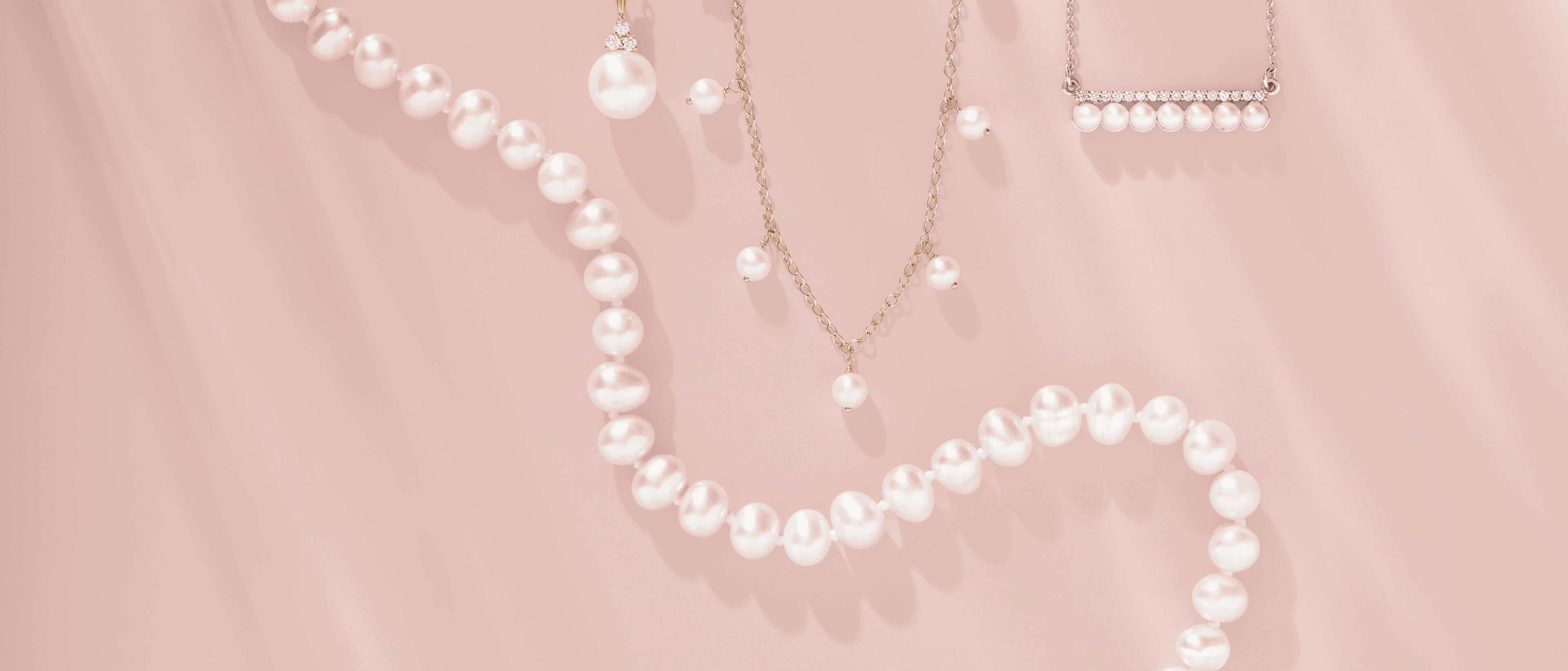 Assorted pearl jewelry, such as a string, two necklaces, and a pendant, against a pink background